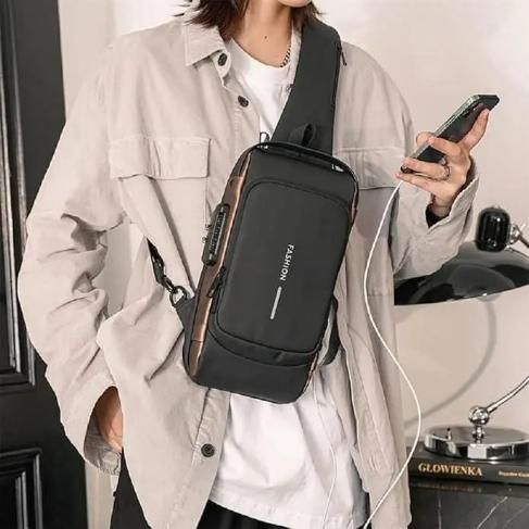 Man wearing beige jacket with black crossbody sling bag, holding smartphone indoors