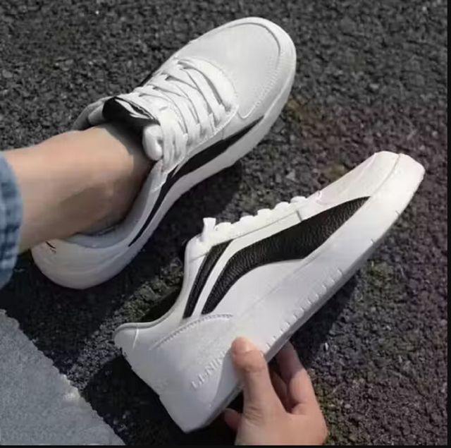 Men's white low-top sneakers with a bold black side panel, featuring flat white rubber soles