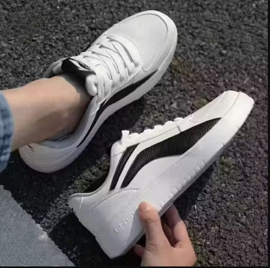 Men's white low-top sneakers with a bold black side panel, featuring flat white rubber soles