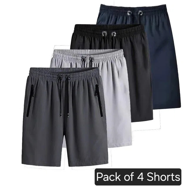 A set of four men's athletic shorts in charcoal, grey, black, and navy blue, showcasing elastic waistbands, drawstrings, and vertical zipper side pockets.
