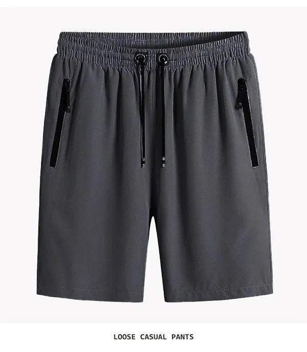 A set of four men's athletic shorts in charcoal, silver, black, and navy blue, showcasing elastic waistbands, drawstrings, and vertical zipper side pockets.